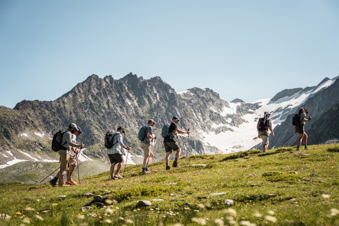 A group hiking across a green field with snowy mountains in the distance.